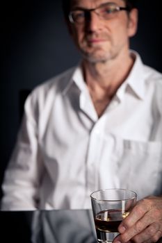 adult man holding an alcoholic drink thoughtful on black background