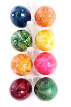 Overhead view of eight different colourful marbled Easter Eggs in a box on a white background