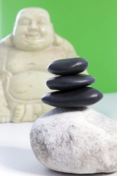Three black stones stacked on top of a larger grey speckled stone with a Buddha statue in the background.