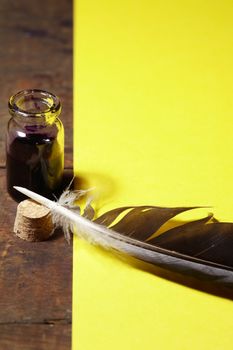 Vintage still life with inkpot and feather on yellow paper background