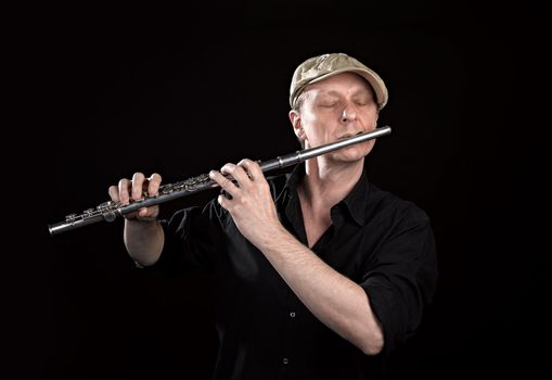 Portrait of a man playing old silver transverse flute on black background