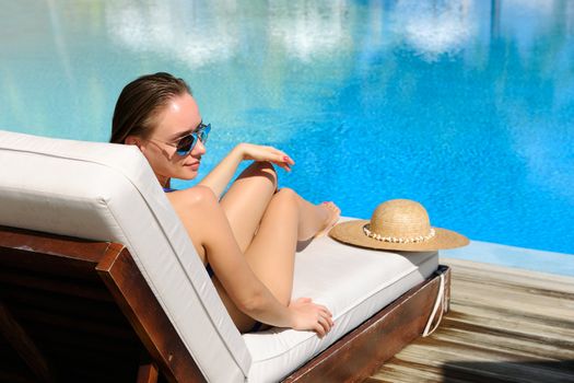 Woman relaxing in chaise lounge at the poolside 