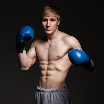 Young handsome boxer in blue gloves over dark background