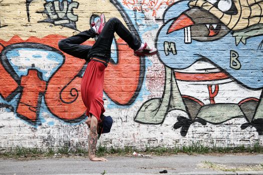 A performing HipHop Dancer in front of a Graffiti wall.