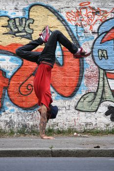 A performing HipHop Dancer in front of a Graffiti wall.