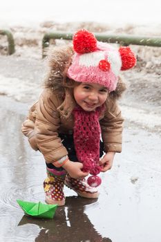 Little girl plays with paper ships in a spring puddle