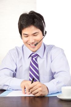 Asian businessman wearing a headset sitting at desk isolated on white background.