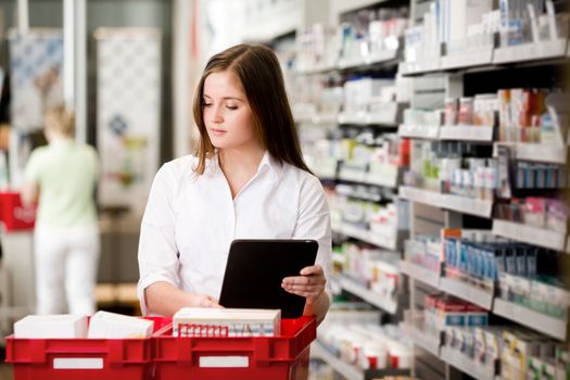 Female pharmacist working in pharmacy with digital tablet and medicine