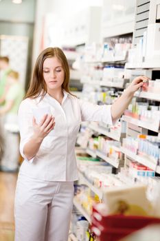 Attractive young pharmacist in pharmacy looking at prescription