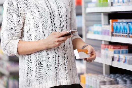 Mid-section of woman holding medication box and dialing on cell phone
