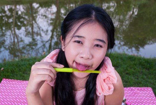 Asian girl is licking jam on plastic knife.