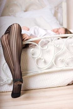 Attractive legs on white bed with fishnet stockings and high heel shoes.