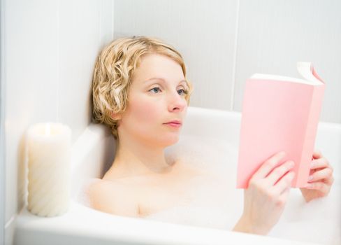 Young woman relaxing and reading a book in the bath with candlelight
