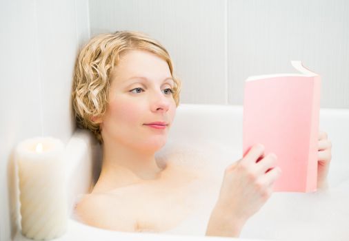 Young woman relaxing and reading a book in the bath with candlelight