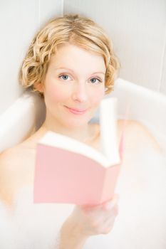 Hayy young woman relaxing and reading a book in the bath