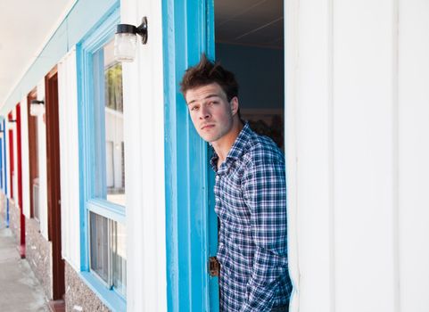 Worried young man looks out of the ugly motel room