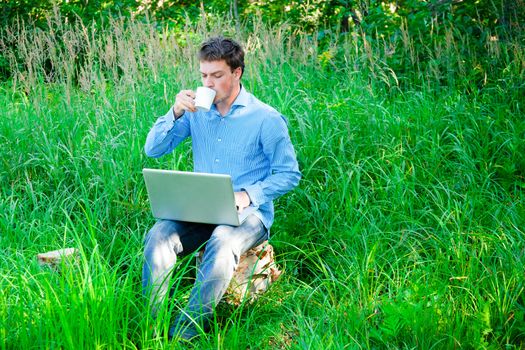 Young man working outdoors with a cup and laptop