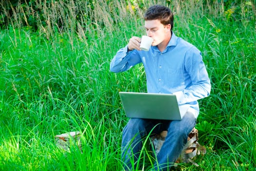 Young man working outdoors with a cup and laptop