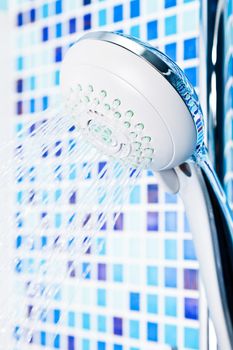 Shower head with running water against blue tiled bathroom wall