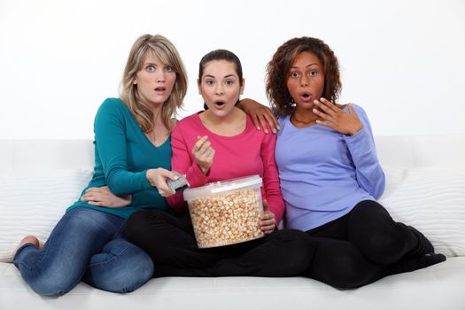 Three women eating popcorn whilst watching film
