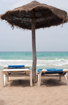 Two chaise longes on the beach and parasol