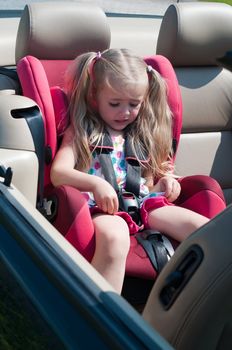 Little cute girl with long blond hair sitting in car seat