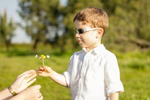 Happy cute son giving a bouquet of flowers to his mother in a sunny field