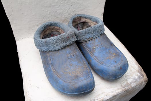 Old dirty galoshes standing on the concrete floor near the wall 