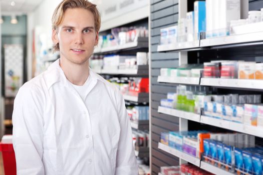 Portrait of male pharmacist standing in drugstore near the shelf