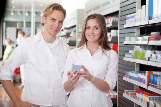 Two Pharmacists With Pharmaceuticals In Hand Consulting Each Other In A Pharmacy.