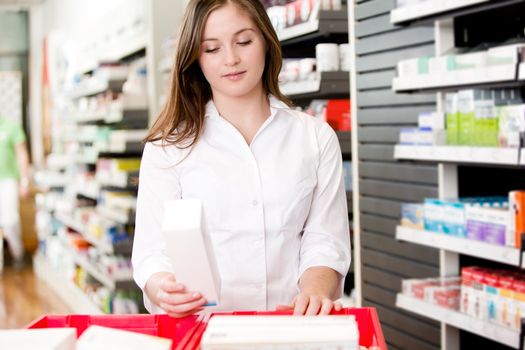 Pharmacist stocking shelves in pharmacy with box of medicine