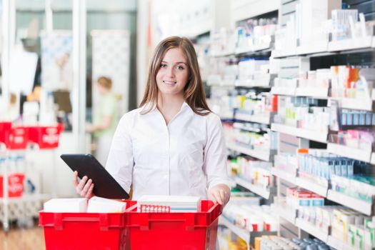 Portrait of female chemist holding tablet PC standing with basket at drugstore