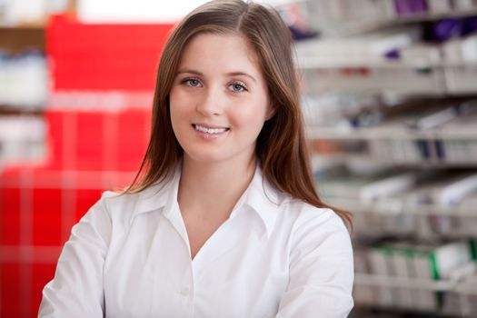 Portrait Of A Female Pharmacist At Pharmacy, In Front Of Shelves With Pharmaceuticals.