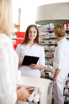 Portrait Of Female Pharmacist Holding Tablet Pc While Attending Customer.