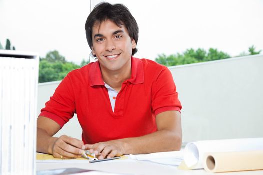 Portrait of young male architect smiling while working on a blueprint