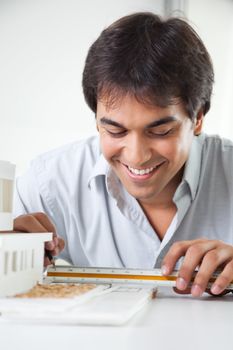 Skilled young male architect completing a design at the drawing board with ruler