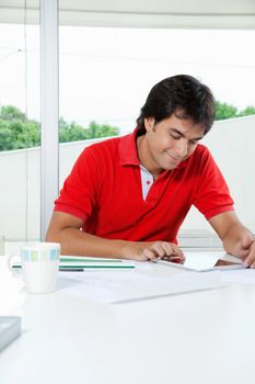 Youngman in casual t-shirt using digital tablet while sitting at desk