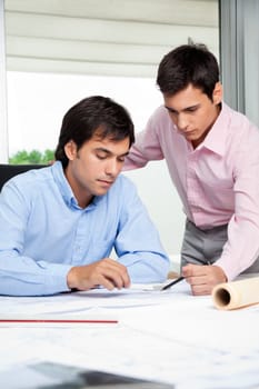 Young male architects working on blueprint together in office