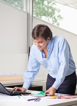 Male interior designer in office using laptop with color swatch.