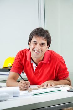 Portrait of young male architect drafting blueprint while sitting at desk