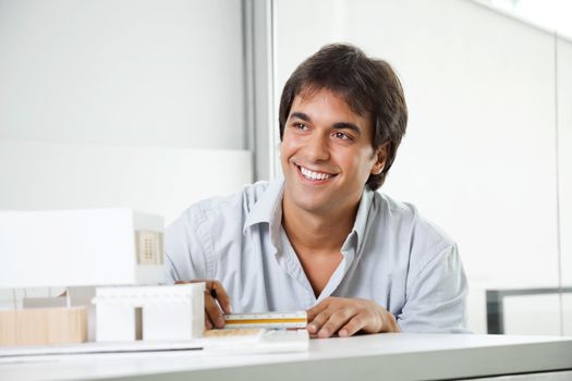 Happy young male architect looking away while creating a model house