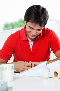 Young male architect in casual t-shirt smiling while working on blueprint