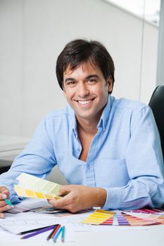 Portrait of young male interior designer smiling while holding color swatches