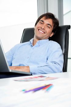Portrait of happy young male interior designer using laptop