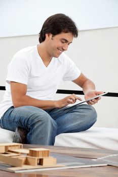 Young male architect in casual wear using tablet PC with model structure on tablet