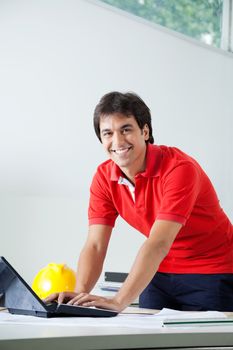 Portrait of young male architect in casual wear smiling while working on laptop