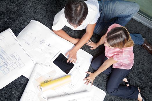 High angle view of couple sitting on rug with blueprints and digital tablet