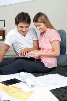 Young couple selecting color from swatches while sitting on rug with blueprints and digital tablet