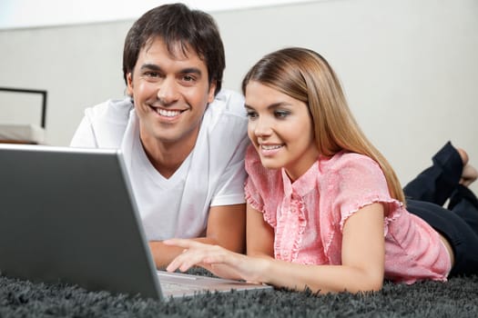 Portrait of young couple lying on rug comfortably with laptop