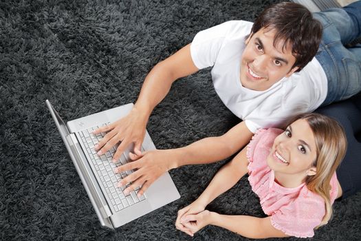 High angle view of young couple lying on rug with laptop